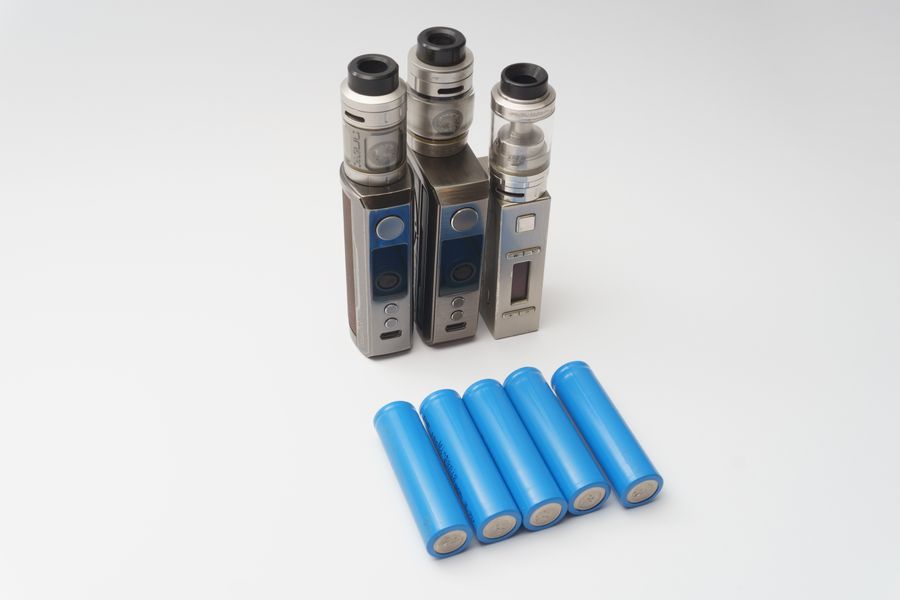 Box mods and spare batteries on a white surface