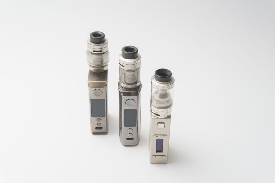 Three box mods with sub-ohm tanks, standing on a white surface